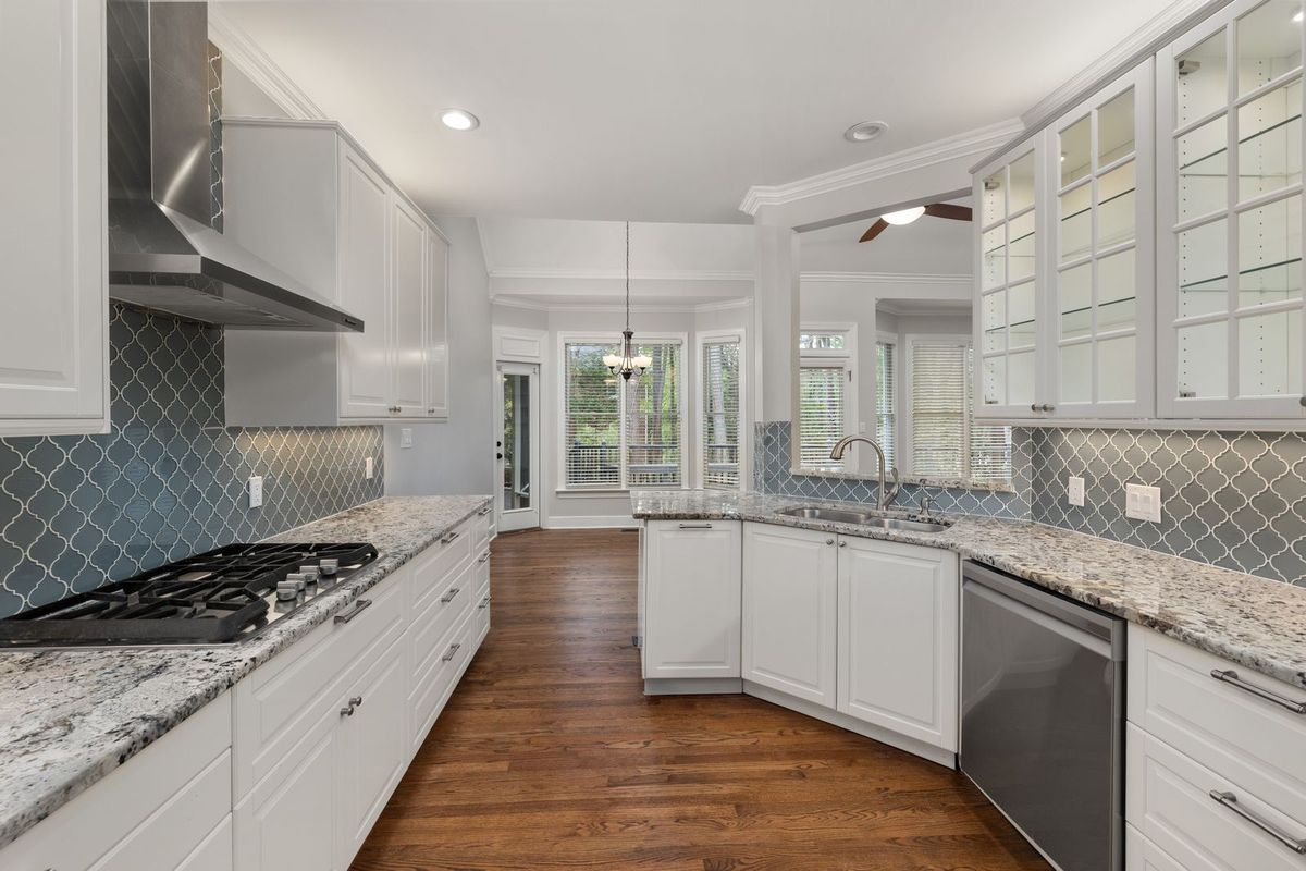 White kitchen with glass-front cabinets, a blue arabesque tile backsplash and wood floors