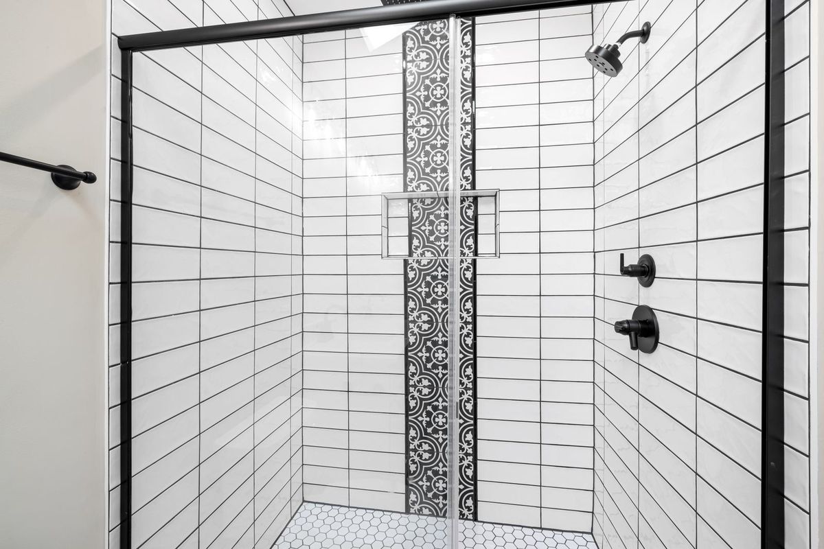 Walk-in shower with white subway tile, a patterned accent strip and black fixtures