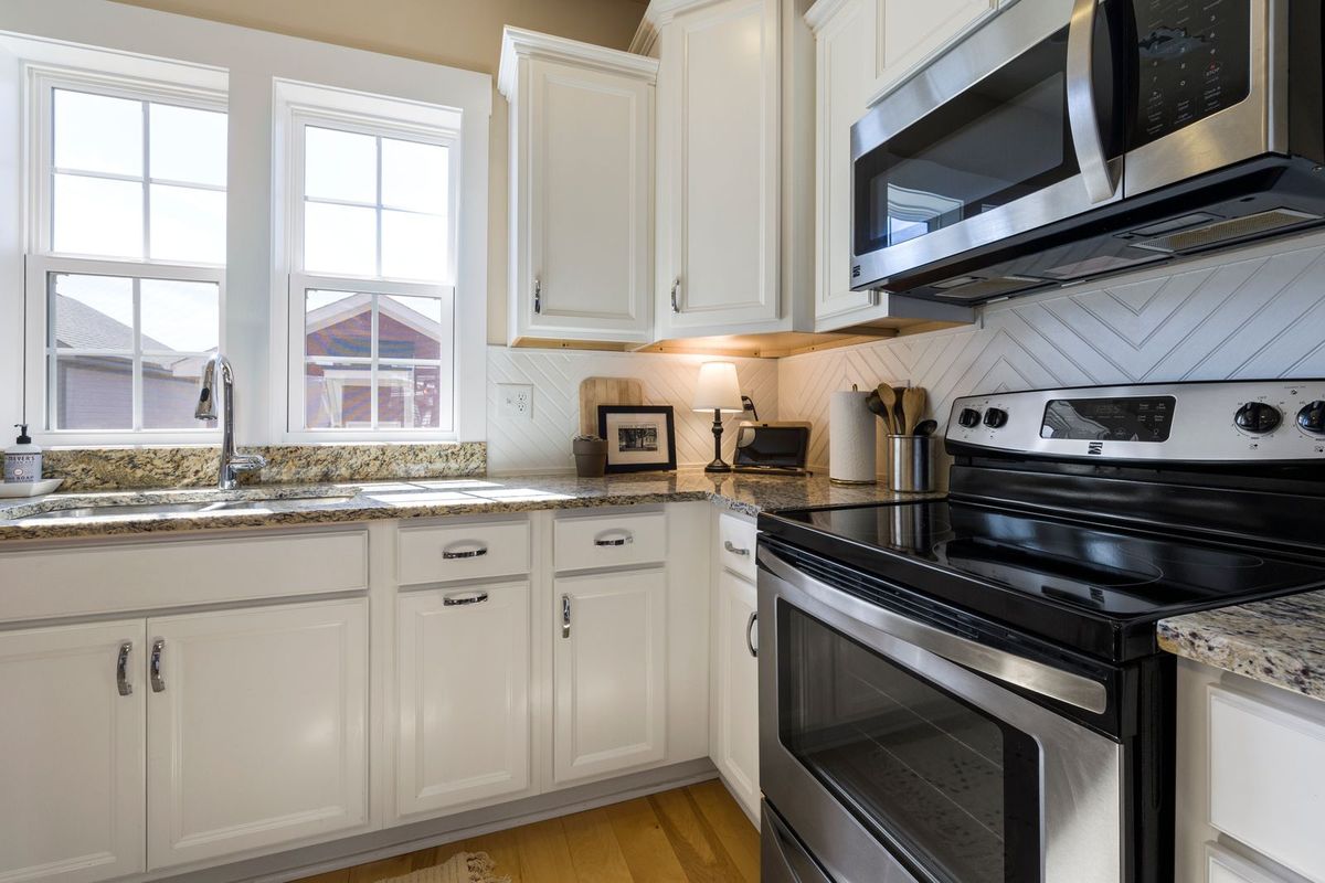 White kitchen cabinets with granite counters under a double window