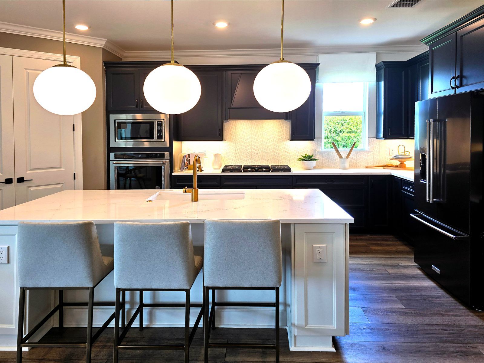 Remodeled kitchen with dark cabinets, a white island and globe pendant lights