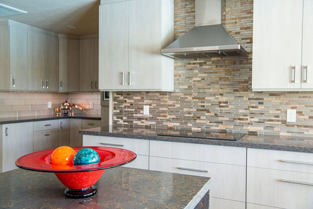 Kitchen with light cabinets, a stainless range hood and a glass tile backsplash